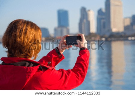 Young woman takes photos using smart mobile cell phone camera of a downtown San Diego City. Women caucasian tourist use mobile phone take a photo landscape San Diego. Mobile photograph and video.