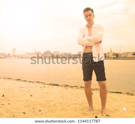 A young guy in a white shirt is on the beach near the river in the city. Sunset

