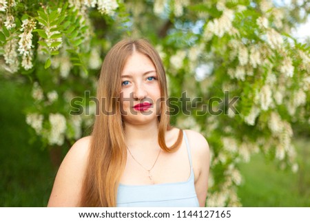 portrait of a girl long hair with plus size figure surrounded by blossoms acacia on a green spring meadow