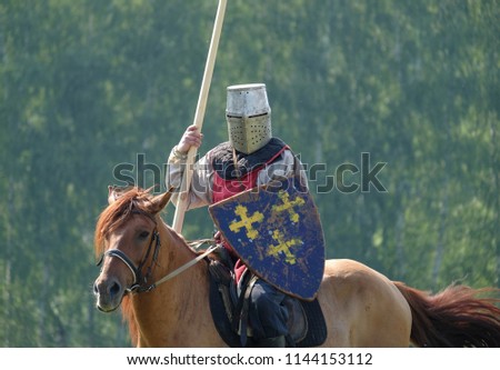 medieval knight with a spear riding a horse on a background of green forest in the field. historical reconstruction