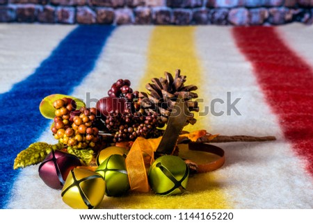 isolated small bells in fall colors with orange ribbon autumn berries pine cone and acorn on white wool blanket with red blue and yellow stripes with room for print