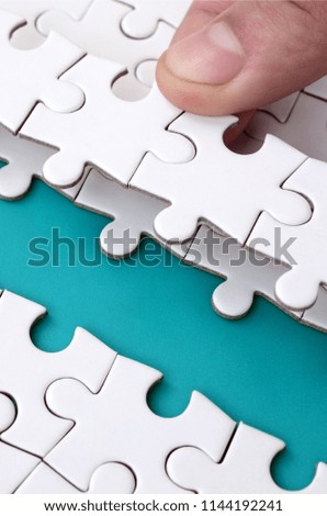 The human hand paves the way to the surface of the jigsaw puzzle, forming a blue space. The concept of overcoming the difficulties on the way to success