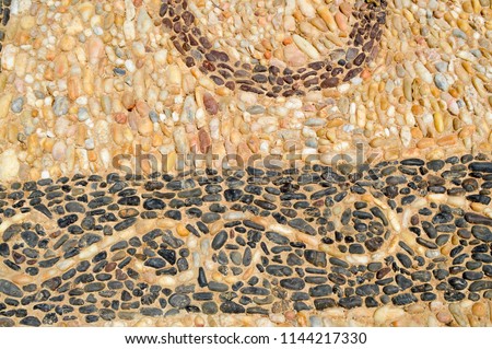 The texture of the stone wall, the road from small round and oval stones with abstract lines laid out patterns of sandy seams of natural old yellow black brown. The background.