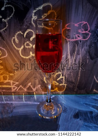 Wine glass with an alcoholic drink, red wine. Dark black wooden chalk flowers background with bright orange, blue light. Art work romantic.