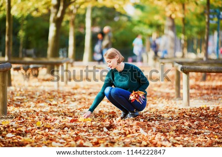 Beautiful young woman gathering colorful autumn leaves while walking in park on a fall day. Luxembourg garden, Paris, France