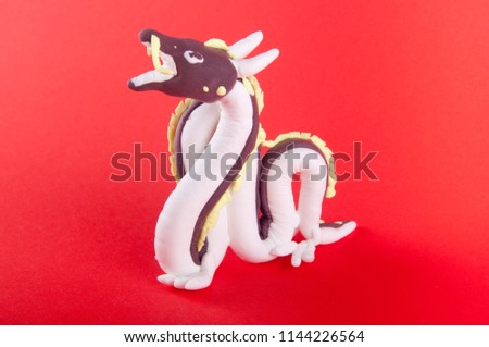 Clay plasticine dragon figure staying on red background. Close up