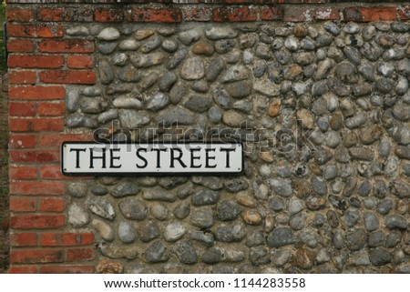 closeup of "the  street" street sign in england on grey small stone cobbled wall with red brick border