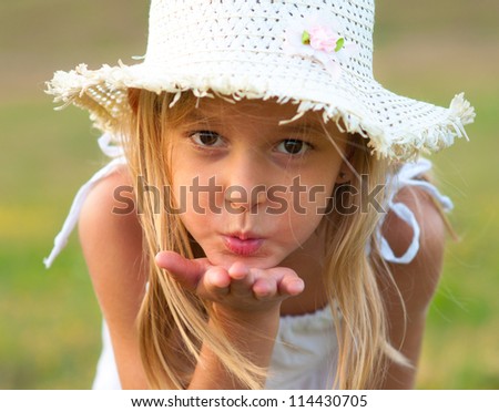 Cute little girl on the meadow blowing a kiss toward you on beautiful summer day.