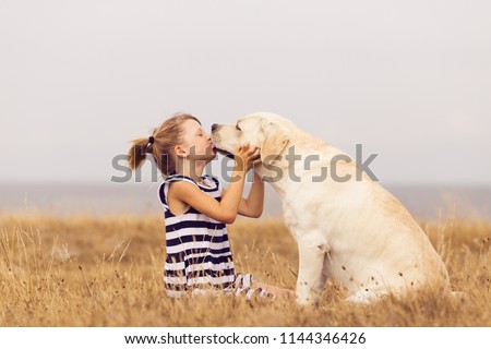 adorable girl hugging her labrador retriever. happy kid with big white dog outdoors. child and her dog best friend having fun in the garden. girl with cute family dog.  Royalty-Free Stock Photo #1144346426