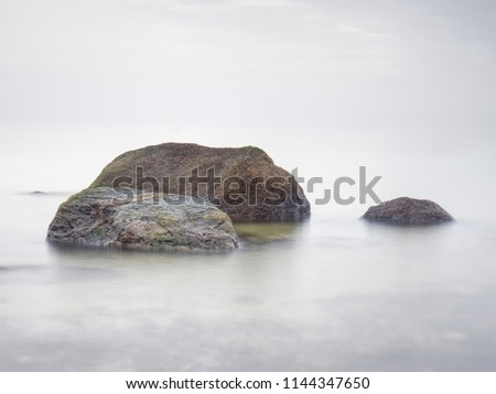 Stony coast defies to waves of ocean clear sky with blurred Sun in high humidity. Smooth evening Sea between stones and horizon. Peaceful Background with Tranquil Calm Water.