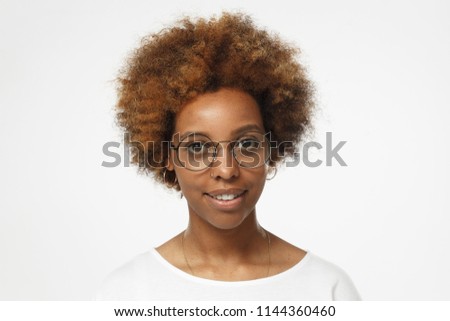 Studio portrait of young smiling african american woman wearing blank white t shirt and nerdy round glasses, isolated on gray background
