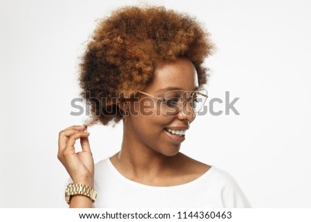 Horizontal closeup headshot of young smiling flirty dark skin african american woman in golden glasses, isolated on gray background, having turned head and touching her hair