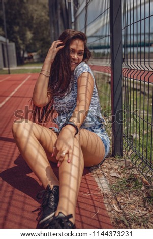 A beautiful smiling Asian Girl posing and having fun in the open. She is sitting on the city basketball court on a beautiful summer day. Looking at camera. 
