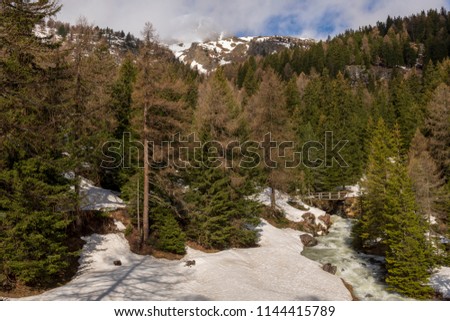 Wooden bridge over a little river in a snowy forest with mountains in background, picture from Switzerland.