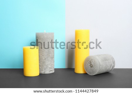 Decorative wax candles on table against color background