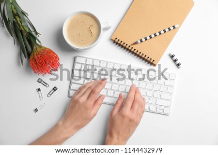 Woman using computer keyboard on white table decorated with tropical flower, top view. Creative design ideas