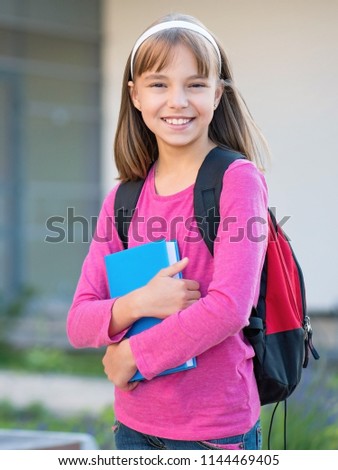 Outdoor portrait of happy child 10-11 years old with backpack, holding books on the first school day. Back to school concept.