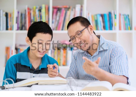 Picture of male teacher guides his student to count while sitting in the library