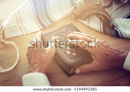 Old Jewish man hands holding a Prayer book, praying, next to tallit and shofar (horn). Jewish traditional symbols. Rosh hashanah (jewish New Year holiday) and Yom kippur concept Royalty-Free Stock Photo #1144492385