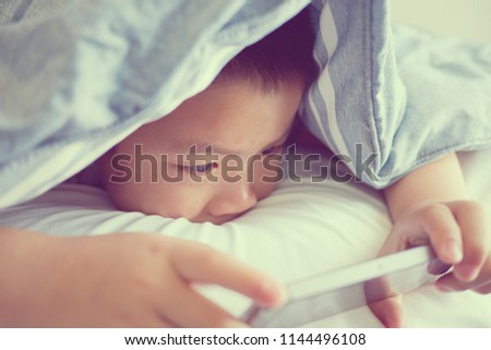 Asian Chinese boy playing smartphone on bed, watching smartphone, kid use phone and play game, child use mobile, addicted game and cartoon, boy play phone
