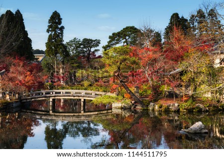 Bridge across pond to shrine surrouned by autumn tree garden with reflection on water at Eikan-do Temple in Kyoto, Japan. Here is famous landmark during fall season.