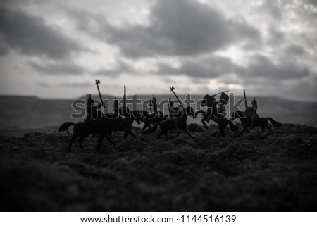 Medieval battle scene with cavalry and infantry. Silhouettes of figures as separate objects, fight between warriors on sunset foggy background. Selective focus