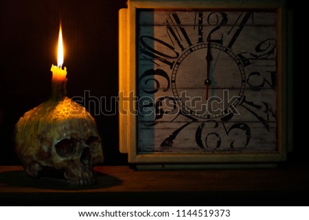 Skull with candle on head and the old clock on the wooden plank in midnight halloween night  / Still life image and space for texts

