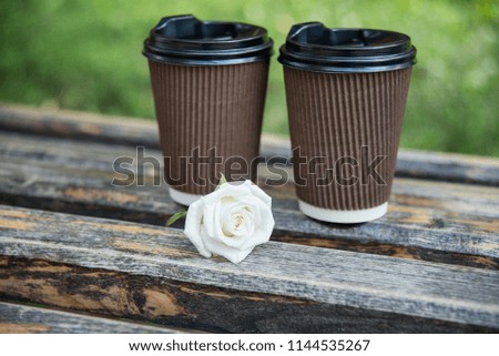 date in the park. 2 cups of coffee and a white rose on a bench. copy space. love, care