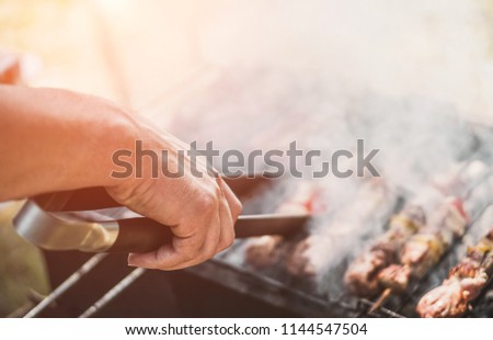 Young man cooking meat on barbecue - Chef cooking some meat skewers on grill in garden outdoor - Summer, food and outside dinner concept - Focus on fingers