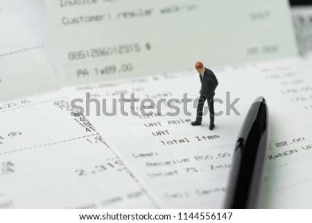 Business expenses, cost or payment concept, miniature businessman figurine standing and checking on company invoice or receipt bills.