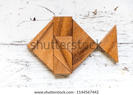 Tangram puzzle in fish shape on old white wood background