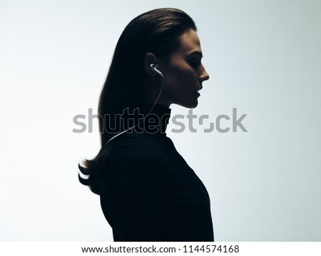 Silhouette of young woman in studio. Side view of female model wearing earphones.