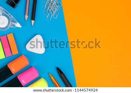 Two pens, two pencils, many paperclips, one eraser, three markers, one correction tape and one clip lie on blue background. Orange background with copyspace Top view.