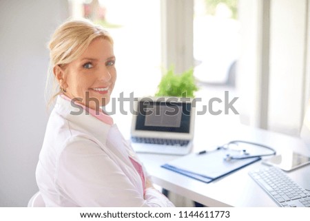 Smiling senior female research physician using computer and laptop while working at desk. 