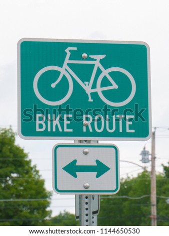 A green bike route sign on the side of the path.