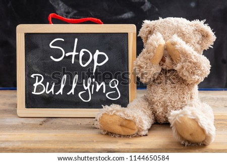 Bullying at school. Teddy bear covering eyes and stop bullying text on a blackboard