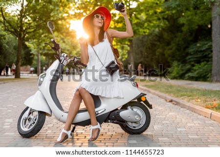attractive woman riding on motorbike in street, summer vacation style, traveling, smiling, happy, having fun, stylish outfit, adventures, taking pictures on vintage photo camera