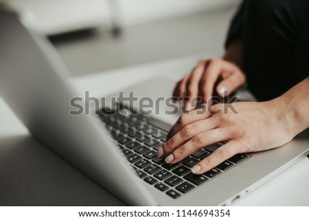 A picture of girl's hands typing message on laptop. She works. Laptop is grey. It is on white table