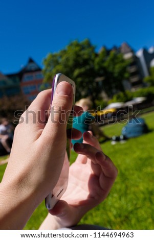 Young girl with painted nails typing on her mobile phone in a park. Close up on hands holding cell phone. Green grass in the background.