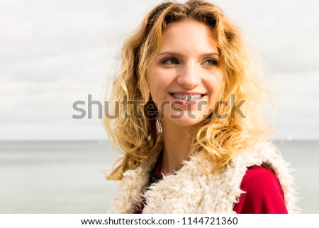 Happy smiling blonde woman portrait. Joyful female being positive walking outdoor wearing fur vest.