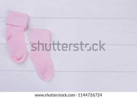 Pink pair of baby socks with copy space. White wood background.