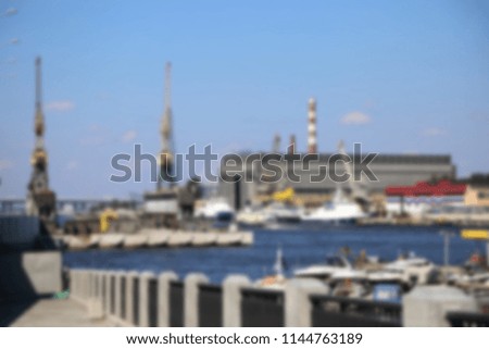 blurred background with urban landscape on river, plant and construction cranes