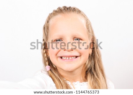 First person view of cute blonde four year old girl with funny pigtail and beautiful blue eyes taking selfie on smartphone. Childhood & technology concept. Adorable little child. Copy space background