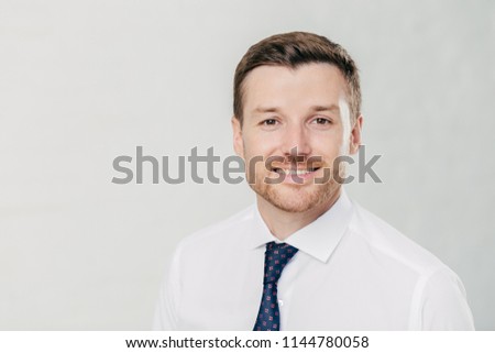 Headshot of attractive unshaven young male with cheerful expression, looks confidently at camera, being pleased to meet with colleagues, dressed in formal clothes, isolated over white background Royalty-Free Stock Photo #1144780058