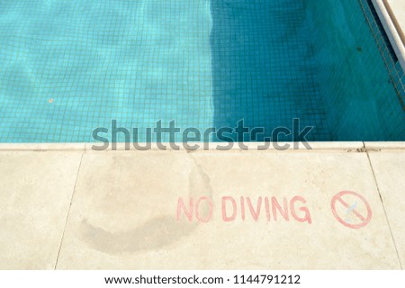 Red paint inscription no diving for safety on the background of the pool on a tropical warm sea resort and copy space.