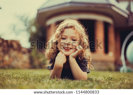 Little cute blonde girl posing in the yard on the grass in summer
