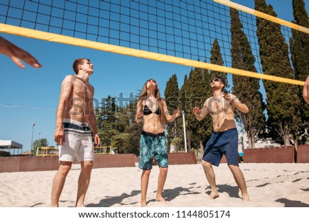group of fit cheerful guys and girls, dressed in beach outfit, playing volleyball in sunny day during their summer holidays.