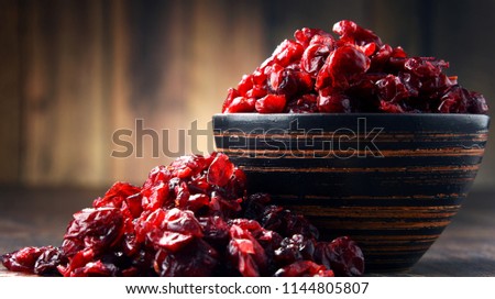 Composition with bowl of dried cranberries on wooden table.
