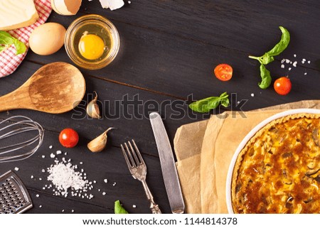 Homemade quiche lorraine with chicken, mushrooms and cheese, kitchenware and ingredients for cooking black wooden background. French cuisine