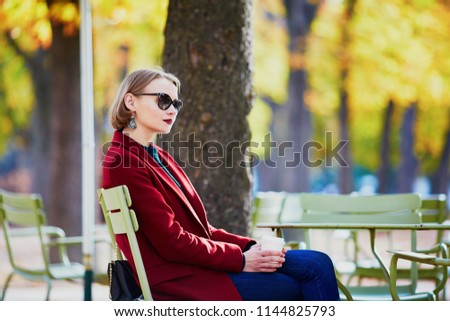 Elegant Parisian woman drinking coffee in park on a bright sunny autumn day